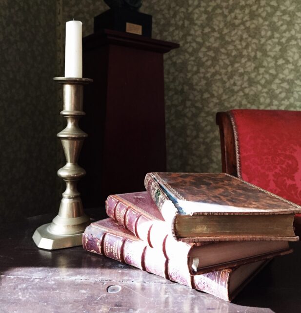 Picture of one brass candlestick on a table next to a pile of books in the Aaron Burr bedchamber.